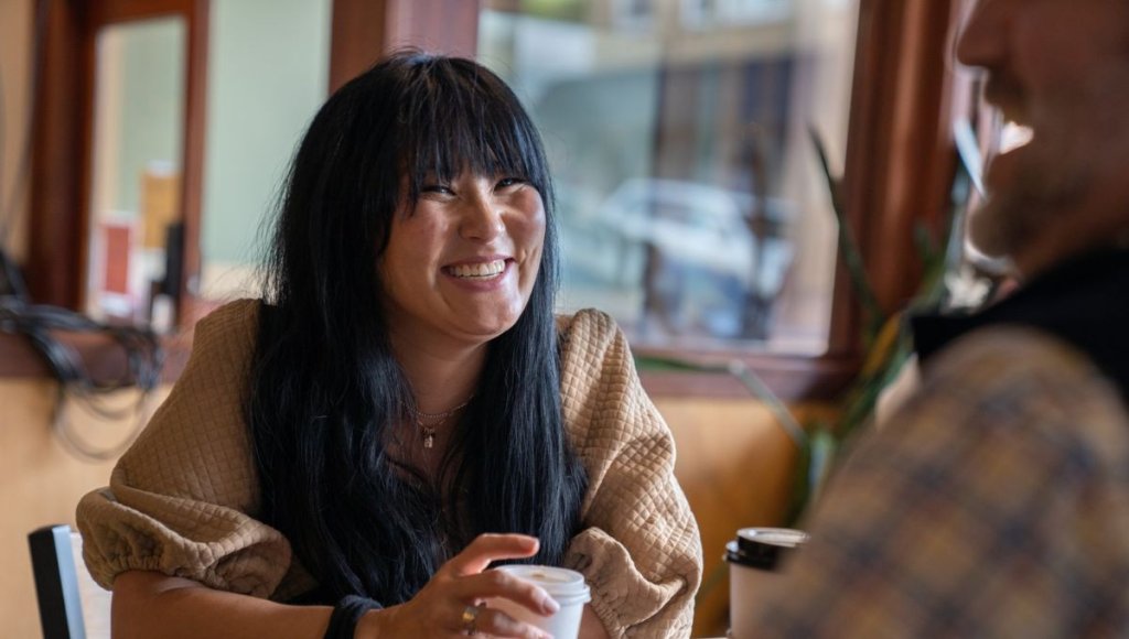 Woman with a cup of coffee with the Wild Bean, smiling at the man in front of her.
